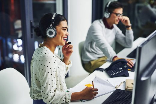 Happy business professionals talk on their headsets while working at their computers
